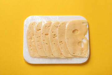 Pack of sliced cheese on yellow background, top view
