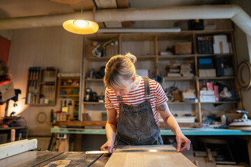 Female carpenter checks wooden beam flatness with ruler in workshop, verifying alignment. Joiner preparing for cutting process, manual woodworking, meticulous attention to detail before production
