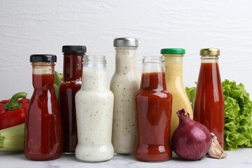Tasty sauces in glass bottles and fresh products on white marble table, closeup
