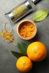 Orange zest, grater and fresh fruits on gray textured table, flat lay