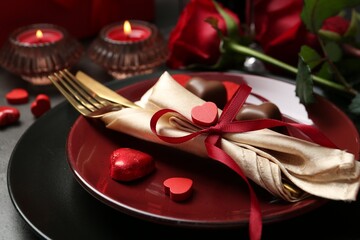 Romantic place setting for Valentine's day. Tableware, cutlery, candies and decorative hearts on grey table, closeup