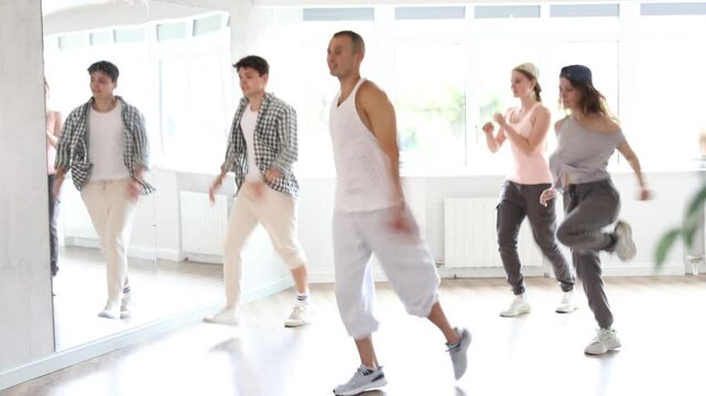 Young man standing performs basic hip hop movements in front of group of students. Developing precise movements, rehearsing arc elements, nae nae moving 
