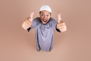 High Angle Full Body Shot Of Attractive Asian Muslim Man Showing Thumbs Up Isolated On Beige...