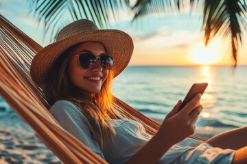 Remote work Joyful young woman in a straw hat and sunglasses uses her smartphone while relaxing in a beach hammock at sunset balancing vacation with her job