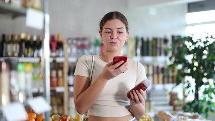 Young woman buyer scanning qr code for red smoothie in bottle in grocery store 