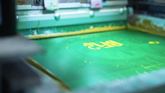 Detailed closeup of automated screenprinting setup applying ink on fabric, precise and detailed vibrant design in action