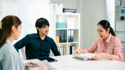A professional meeting takes place with three individuals discussing documents at a modern workspace, showcasing collaboration and teamwork.