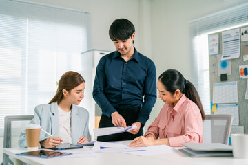 Obraz premium Three professionals collaborate in a modern office, discussing documents and sharing ideas while seated at a table with coffee and digital devices.