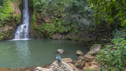 Waterfall. The stream flows down a sheer cliff into a turquoise lake. Tropical vegetation on the...
