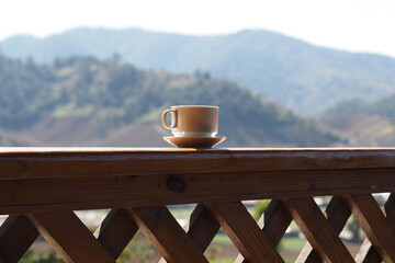 Coffee cup on a wooden table with mountain view during a sunny day.