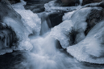 Frozen streaming water in a small river with ice and snow.
