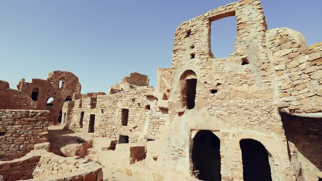 Eroded stone walls and arches of fortifications of Ksar Beni Barka standing under blue Tunisian sky, showcasing traditional Berber architecture in Tataouine