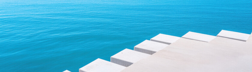 serene view of concrete steps leading into calm blue water, creating tranquil atmosphere. clear water reflects sky, enhancing peaceful setting