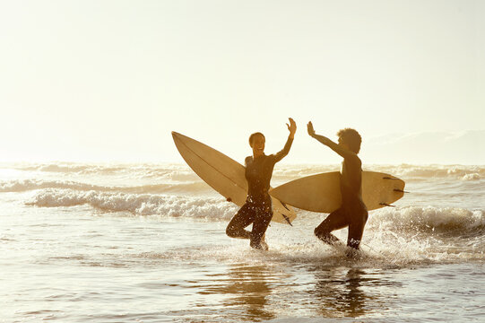 Surfing friends, high five and beach in water with celebration, congratulations and fitness achievement in sunset. Surfer man, woman and sports success on mockup in support for wellness goals by sea