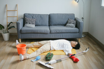 Young Man Lying Down On The Floor With Messy Cleaning Tools 