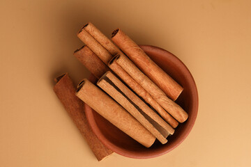 Cinnamon sticks in a earthen  bowl,  on light brown background, selective focus.