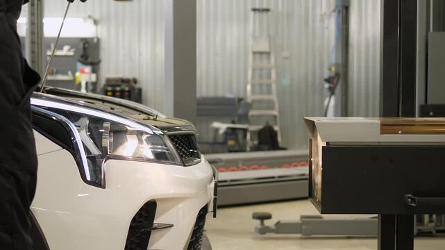 The worker checks and adjusts the headlights of the car's lighting system. Car service. The process of adjusting the headlights with a screwdriver at the service station.
