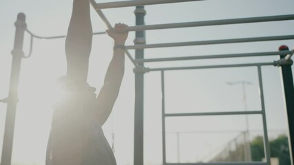 A fit young man working out on monkey bars at an outdoor fitness park, showcasing determination and physical strength under a clear sky. Young Man Exercising on Monkey Bars at Outdoor Fitness Park - Powered by Adobe