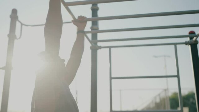 A fit young man working out on monkey bars at an outdoor fitness park, showcasing determination and physical strength under a clear sky. Young Man Exercising on Monkey Bars at Outdoor Fitness Park
