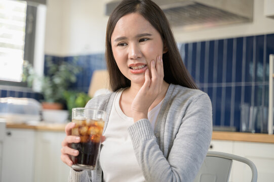 Young Asian woman touching her cheek and mouth feeling pain from toothache, decay or sensitivity cavity molar tooth or inflammation cause by drink cold, sparkling water. Food and health care concept.