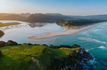 Coastal landscape at sunrise. Sandy spit separating ocean and estuary. Dramatic cliffs and lush greenery. Beautiful New Zealand scenery. Opoutere, Whangamata, Coromandel Peninsula, New Zealand