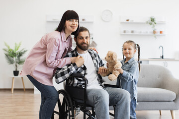 Caucasian family with father in wheelchair interacting warmly with mother and young daughter....