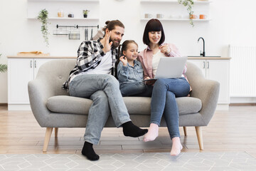 Obraz premium Caucasian family with mother, father, young daughter having video chat on laptop. Happy family bonding and connecting online from modern living room.