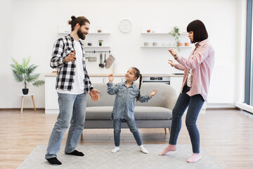 Fototapeta premium Joyful Caucasian family with parents and young daughter dances in modern kitchen. Bright and cheerful home environment emphasizes family bond and happiness.