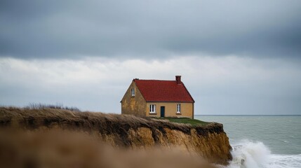 A small house perched precariously on the edge of an eroded cliff in Normandy, France, during high tide. 
