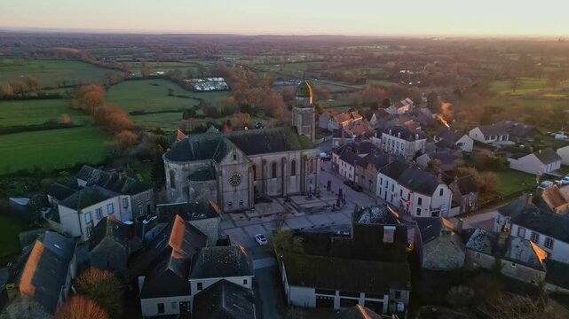 Eglise Saint-Gervais et Saint-Protais, church, Jublains town at sunset, Mayenne in France. Aerial drone forward and cityscape