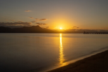 Obraz premium Sunrise over Hinchinbrook Island with a reflection path over the still waters of the channel between Cardwell and the island in this long exposure photo from Cardwell beach in Queensland, Australia.