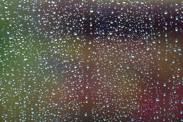 Raindrops on window glass with blurred green nature background in British weather. Crystal-clear water droplets create a natural pattern against a soft bokeh landscape on a rainy day