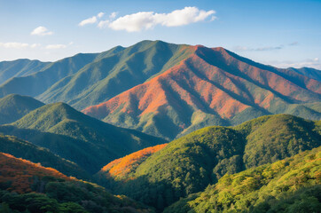 Fototapeta premium Serene Mountain Landscape with Dense Forest Covered in Green and Orange Colors, Clear Sky with Clouds and a Peaceful, Scenic Atmosphere