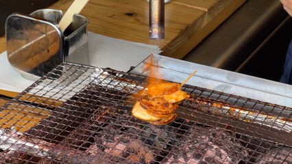 竹串に刺した帆立を醤油をつけてバーナーで焼く