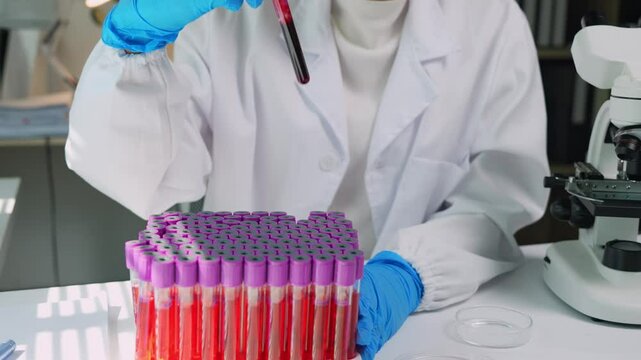 Professional lab technician carefully selecting blood sample from test tube rack during medical research, wearing protective lab coat and sterile gloves for precise scientific analysis