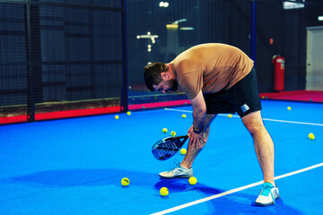 Man practices tennis skills on indoor court with scattered balls in evening lighting