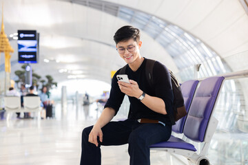 Obraz premium close up young asian man smile and using smartphone with passport ,ticket while sitting in in airport departure area for traveling and people lifestyle concept