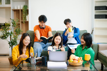 Group of young Asian students working on a project with laptops and tablets. Cozy indoor setting, teamwork,