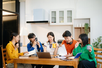 Fototapeta premium Young Asian adults collaborating on laptops and tablets in a cozy workspace, embodying teamwork, c