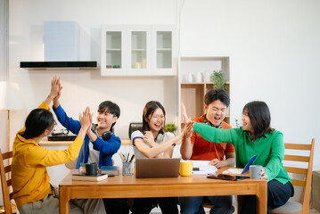 Young Asian adults collaborating on laptops and tablets in a cozy workspace, embodying teamwork, c