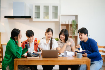 Young Asian adults collaborating on laptops and tablets in a cozy workspace, embodying teamwork, c
