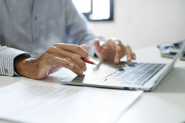 asian businessman using computer laptop working and reviewing document at office workplace. legal expert, professional lawyer reading and checking financial documents or insurance contract