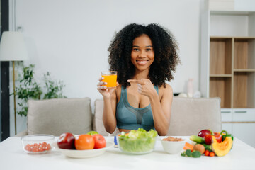 Smiling woman in a modern kitchen with fresh fruits, vegetables, blender, and orange juice, promoting clean eating, wellness