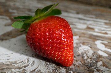 Fresh strawberry glistens under sunlight on rustic wooden surface showcasing nature's vibrant colors