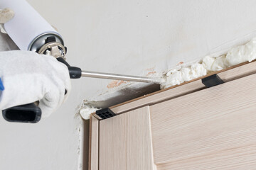 applying foam with a gun into the space between the door frame of an interior door, close-up, hands...