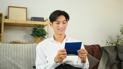 Young man sitting on a couch and reviewing his bankbook. Finance management concept