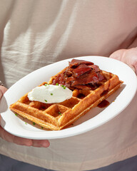 Man holding plate of fresh waffle with beef brisket and cream cheese