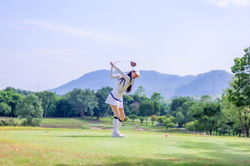  Asian woman happy and fun while playing golf on the golf course. Golfer hitting golf shot with driver club on course. Beautiful woman smiling and holding a golf club while standing on green lawn.