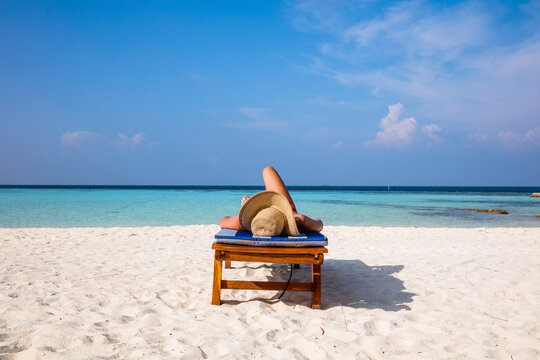 Woman relaxing on lounge chair on the beach, Maldives