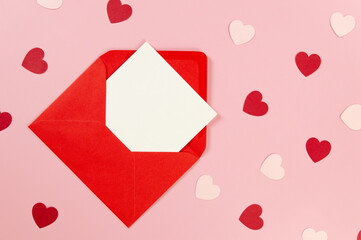 Top view of red envelope, white card on pink background. Pink hearts, red hearts. Valentine's day, love. Post flat lay, copy space.